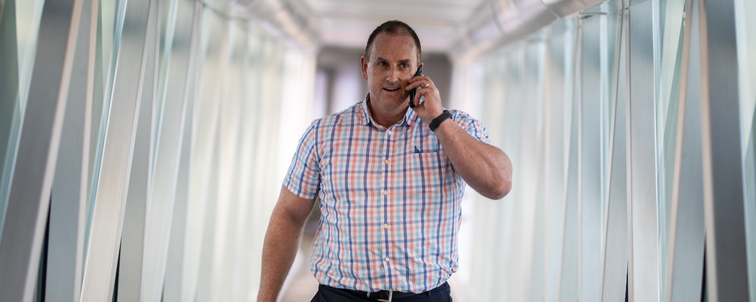 A man walking on an aerobridge while holding a mobile phone.